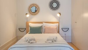 A neatly made bed with a striped bedspread, two bedside lamps, and two wall-mounted mirrors.