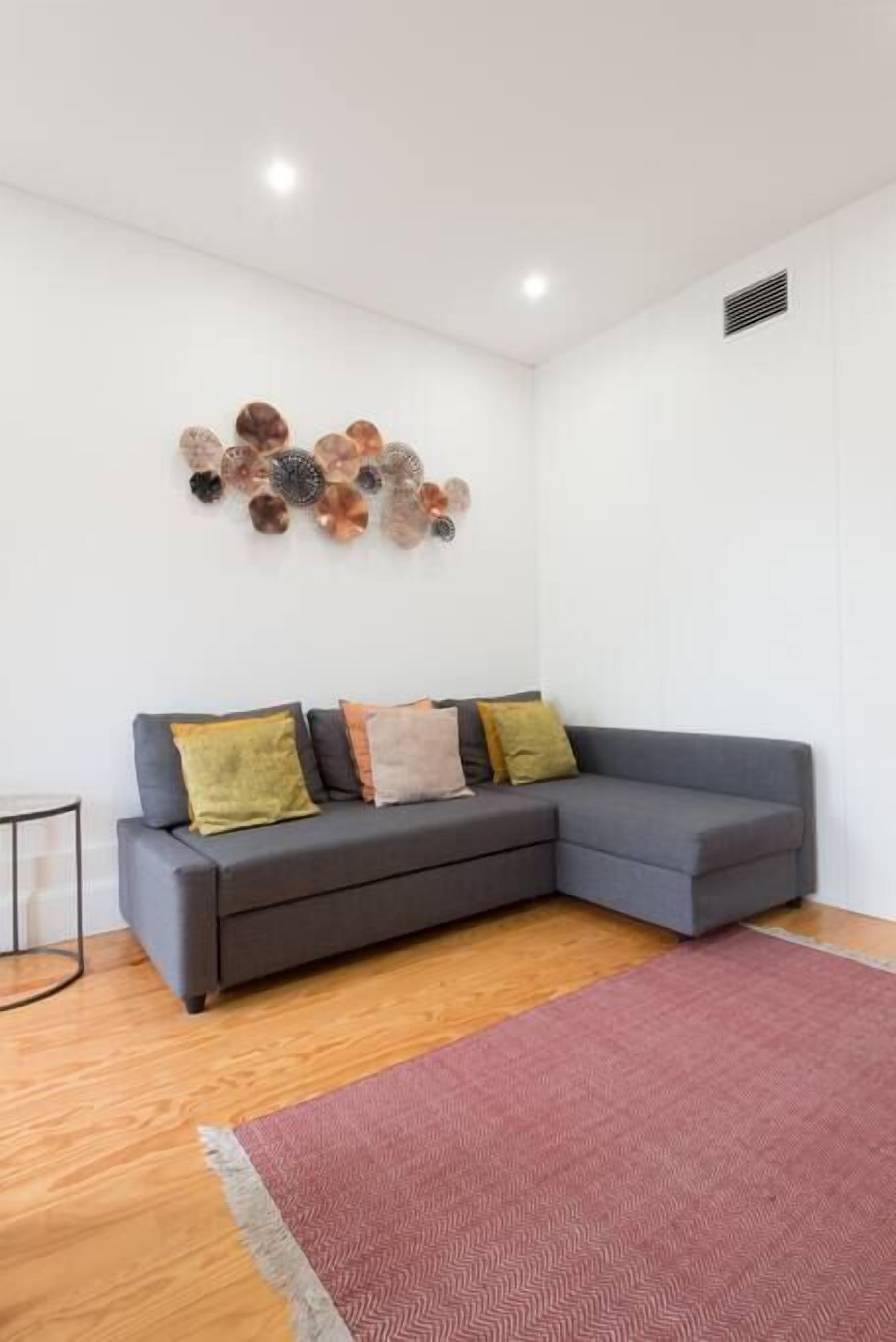 Un salon moderne avec un canapé d’angle gris, un tapis rouge et un élément décoratif mural.