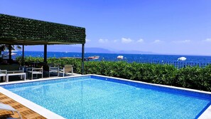 A pool with a view of the ocean, a covered seating area, and a clear sky.