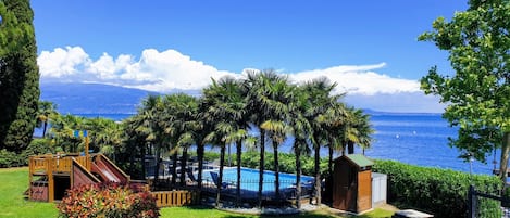 A pool area with a slide, surrounded by palm trees and a view of the sea.
