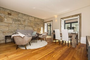 Un salon moderne avec un mur en pierre, un plancher en bois, un canapé, des fauteuils et une table à manger.