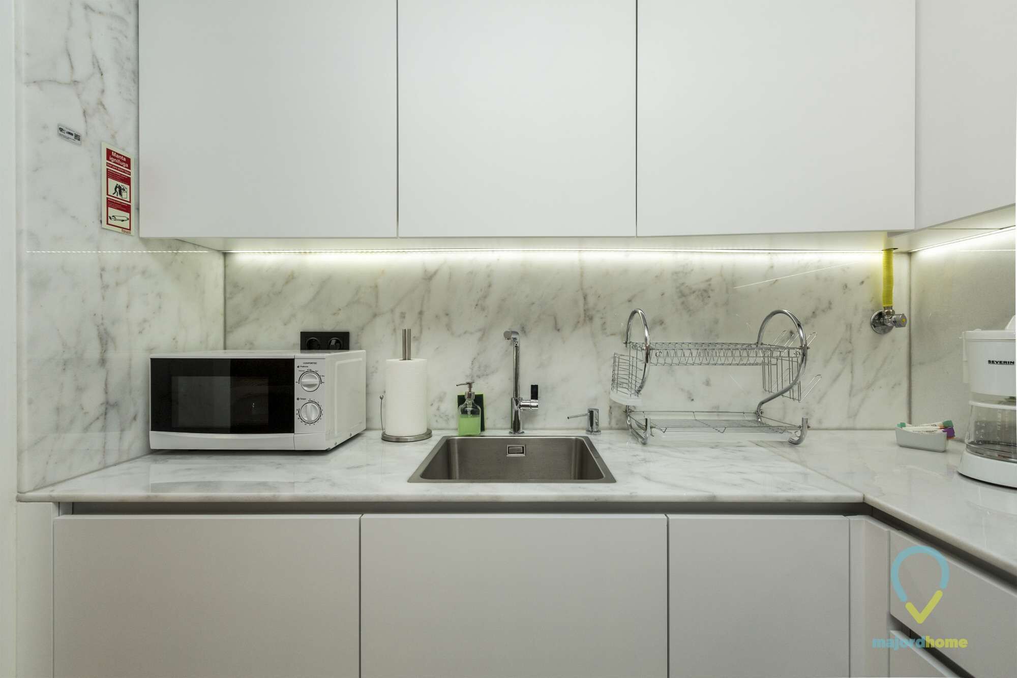Una cocina moderna con armarios blancos, microondas integrado, pileta de acero inoxidable y dispensador de jabón.