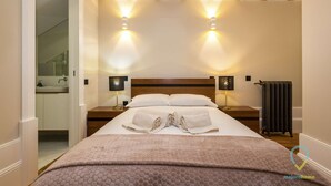 Hotellihuone, jossa on sänky, kaksi yöpöytälamppua, patteri ja kylpyhuone, joka näkyy avonaisen oven läpi.