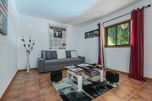 Una sala de estar con un sofá gris, una mesa de centro de cristal con revistas, una cortina roja y un cartel en la pared.