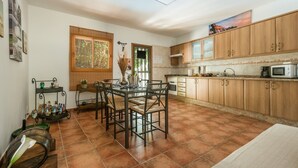 A kitchen with wooden cabinets, a dining table with chairs, a window with blinds, and a microwave. - Vacation Home 'Casa Reina Del Atlántico' with Sea View, Private Pool and Wi-Fi (Candelaria)