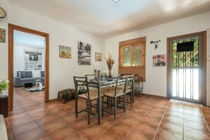 Comedor con una mesa dispuesta para cuatro personas, rodeada de sillas, una ventana con vistas y una puerta que da al exterior.