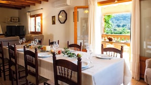 A dining area with a table set for four, wooden chairs, and a view of greenery through a window. - Country house with pool and beautiful views (Cas Concos)