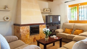 A living room with a stone fireplace, a sofa, a coffee table, and a television. - Country house with pool and beautiful views (Cas Concos)