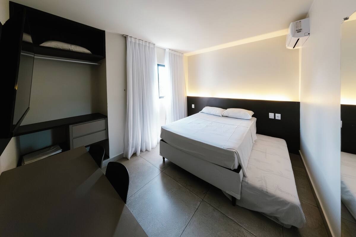 A hotel room with a bed, a desk, a chair, a TV, and a window with curtains.