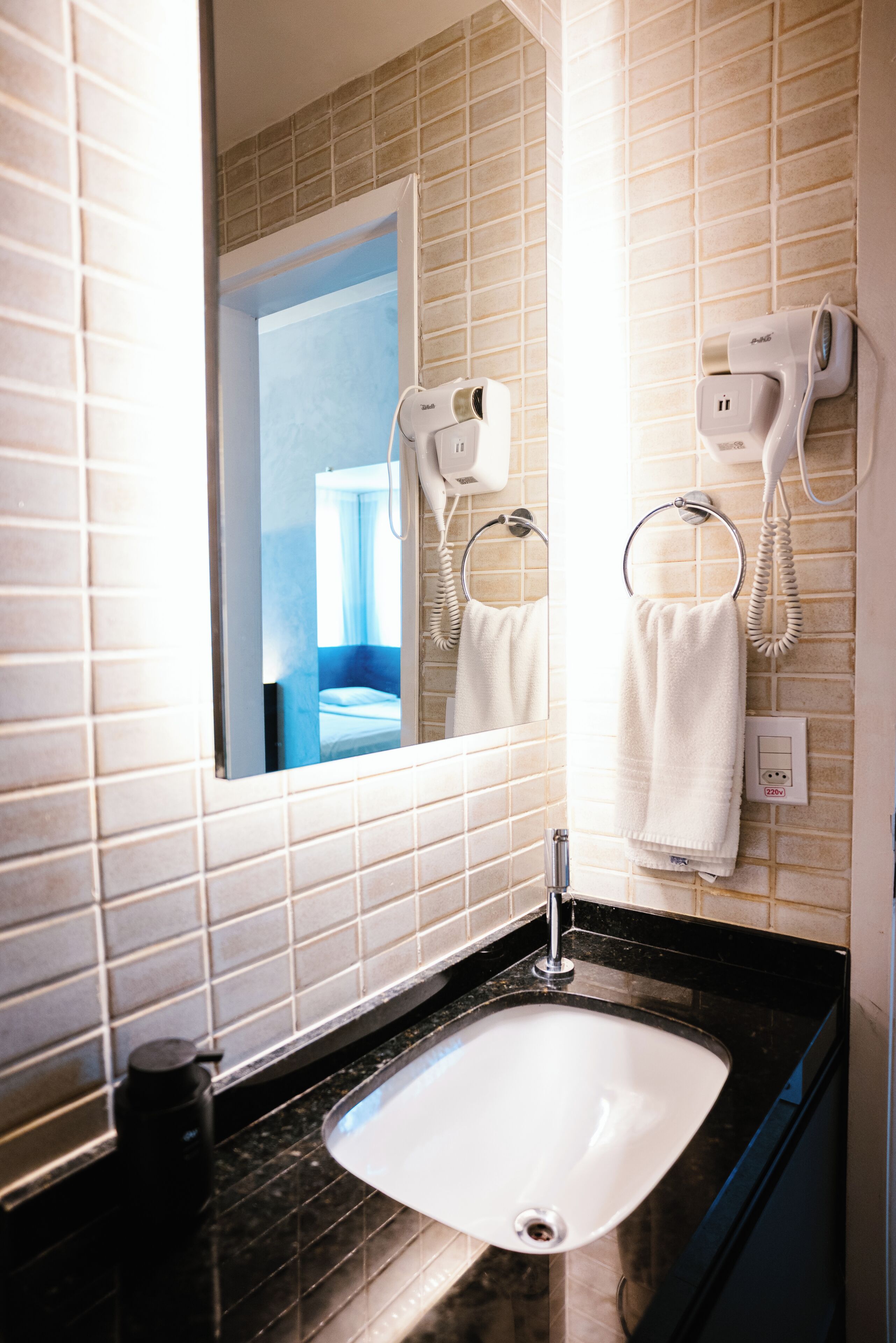 A bathroom with a white sink, a mirror, and two hair dryers mounted on the wall.