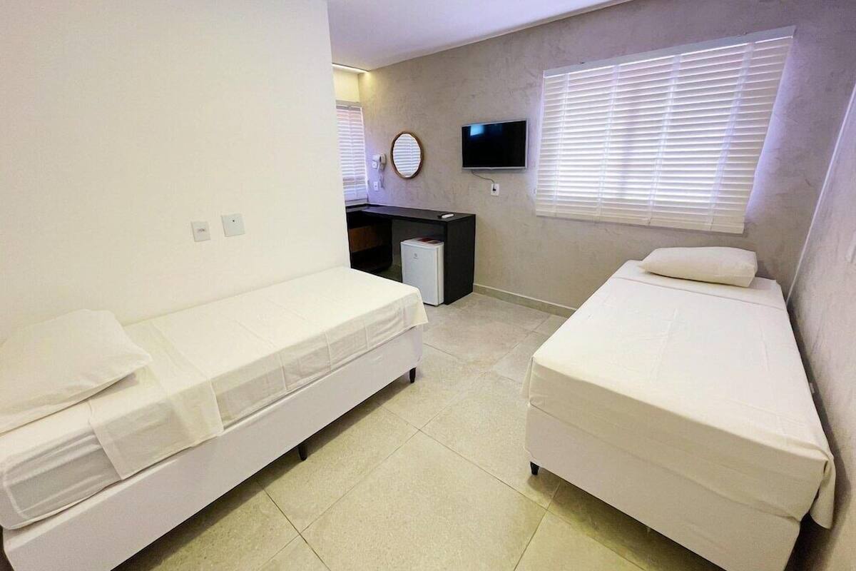 A room with two beds, a desk, a TV, and a window with blinds.