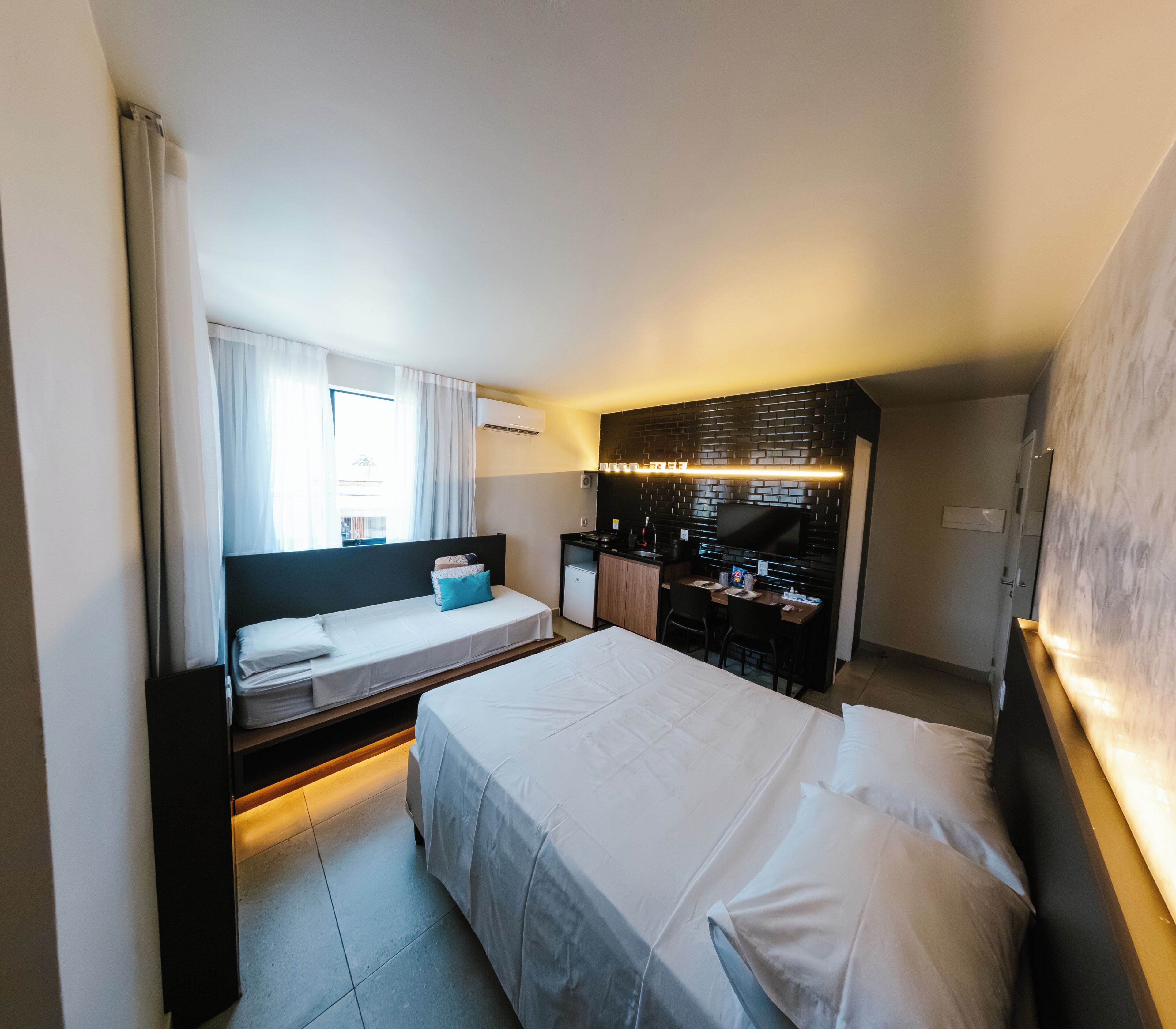 A hotel room with a bed, a desk, a chair, a TV, and an air conditioning unit.