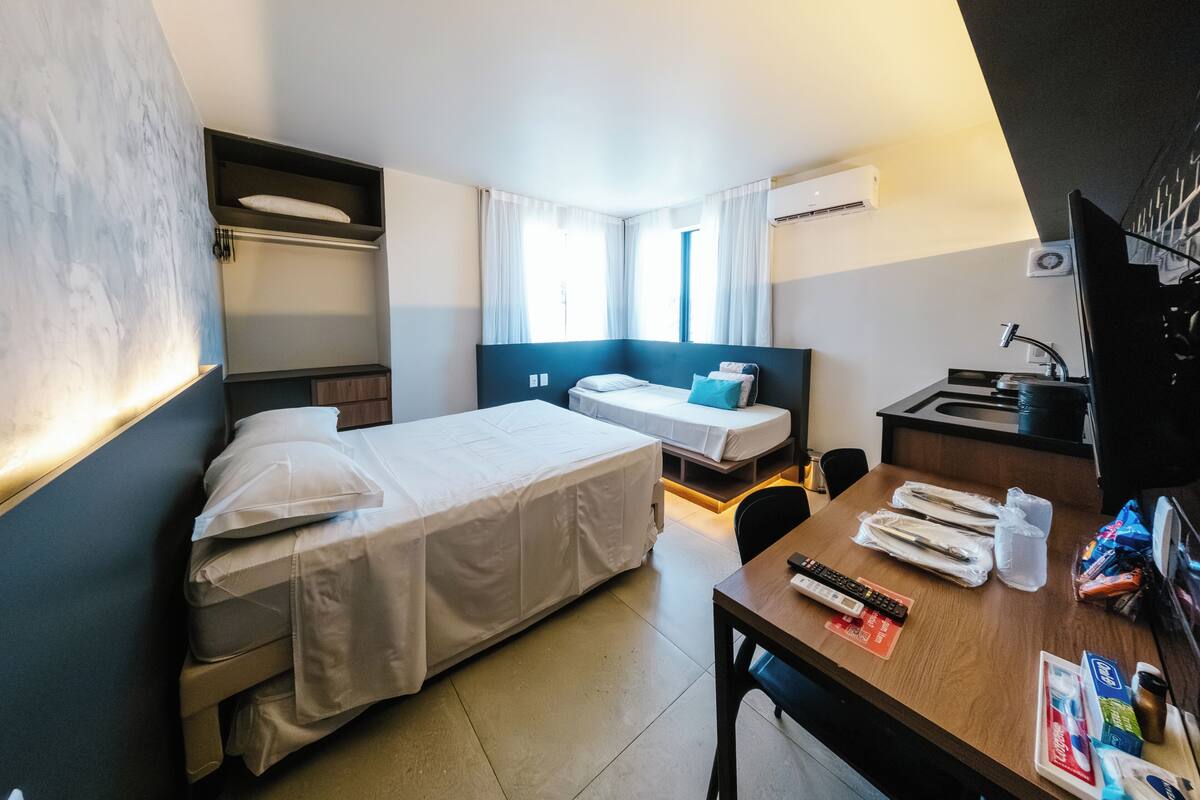 A hotel room with a bed, a desk, a chair, a TV, and a window with curtains.