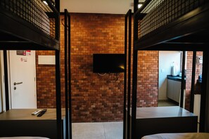 A room with bunk beds, a brick wall, a television, and a door.
