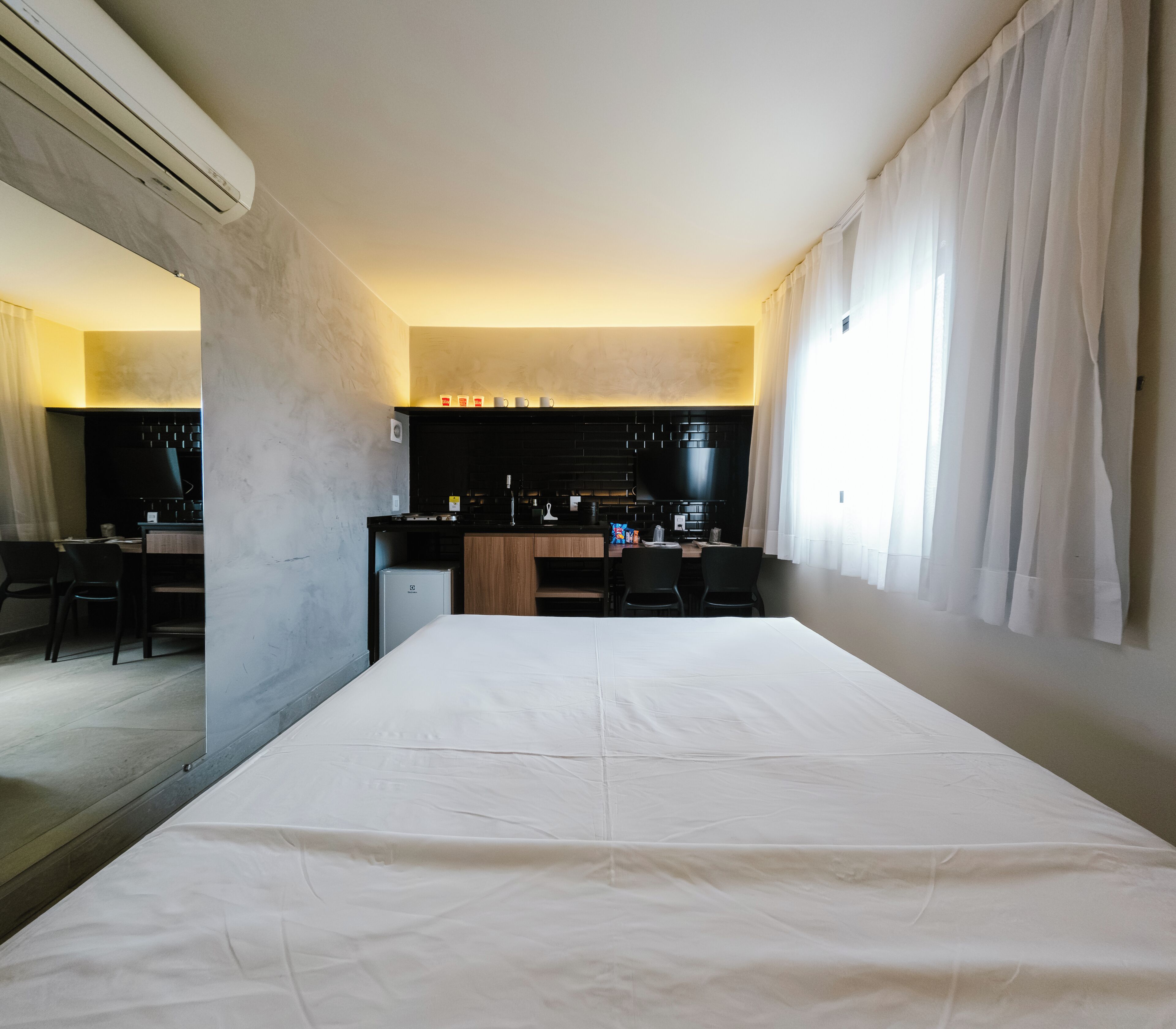 Une chambre d’hôtel comprenant un lit, une kitchenette, un coin repas et une grande fenêtre avec des rideaux.