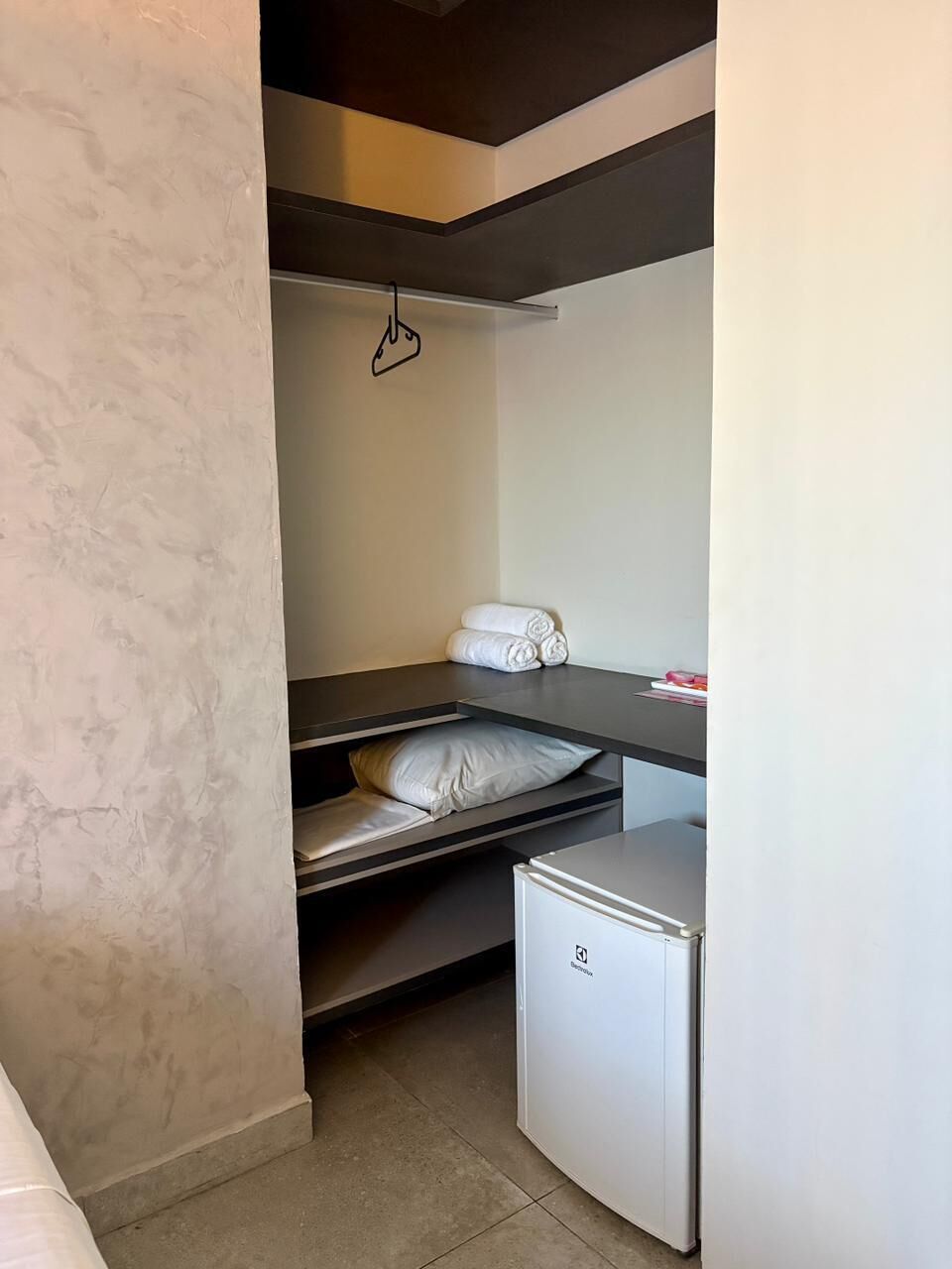 Habitación pequeña con cama, refrigerador y perchero.