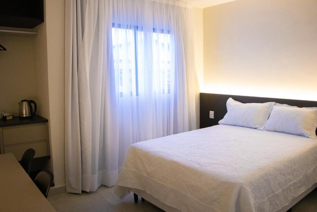 Une chambre d’hôtel avec un lit, un bureau, une chaise et une fenêtre avec des rideaux.