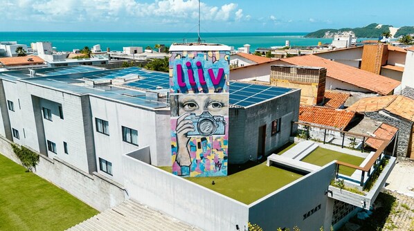 Un bâtiment moderne doté de panneaux solaires, orné d’une fresque colorée et offrant une vue sur la mer.