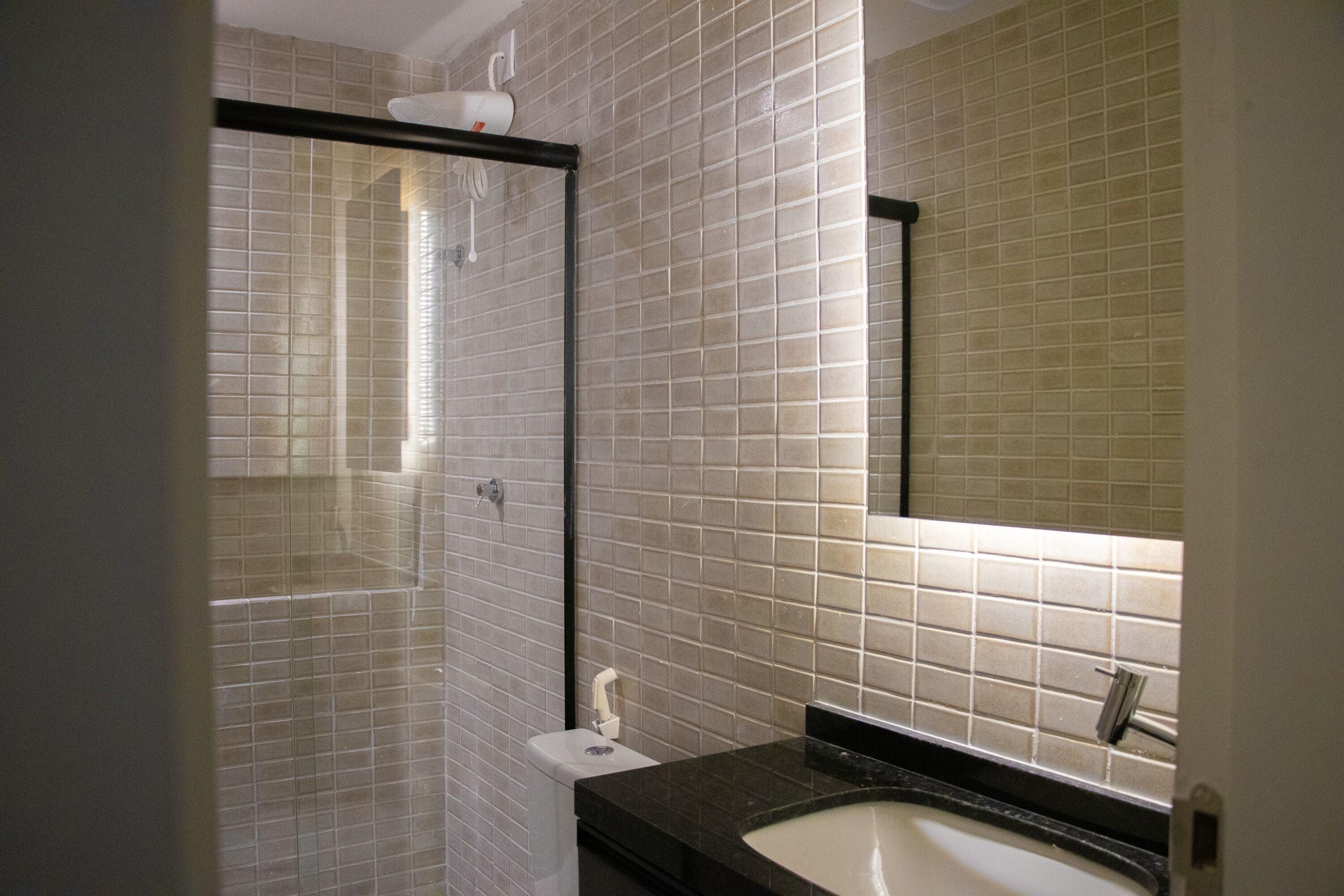 A bathroom with a tiled wall, a shower, a toilet, and a sink with a mirror above it.