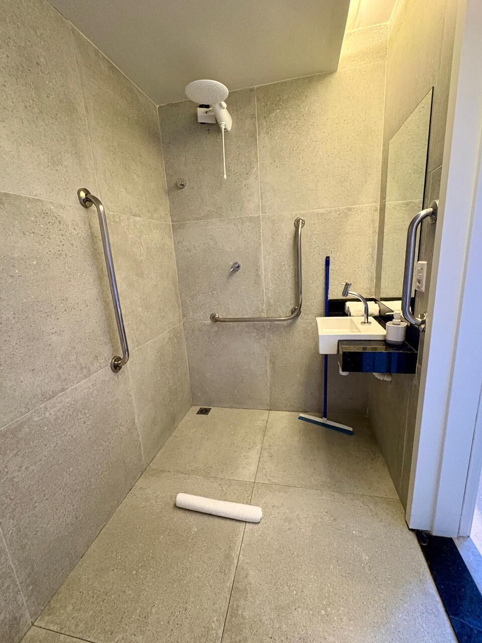 Une salle de bain équipée d’une douche, de barres d’appui, d’un lavabo et de toilettes.