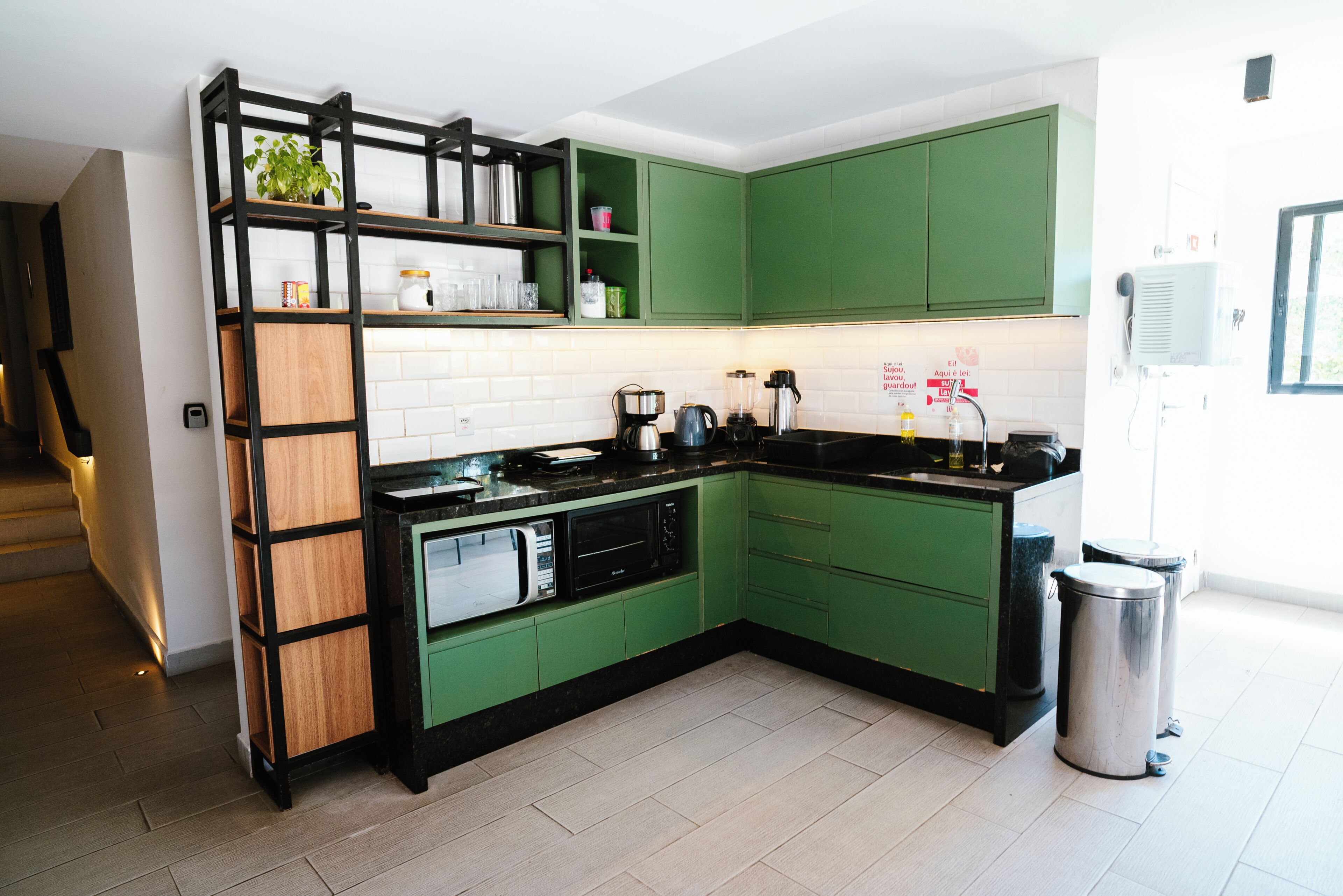 Una cocina moderna con armarios verdes, encimera negra y cubo de basura de acero inoxidable.