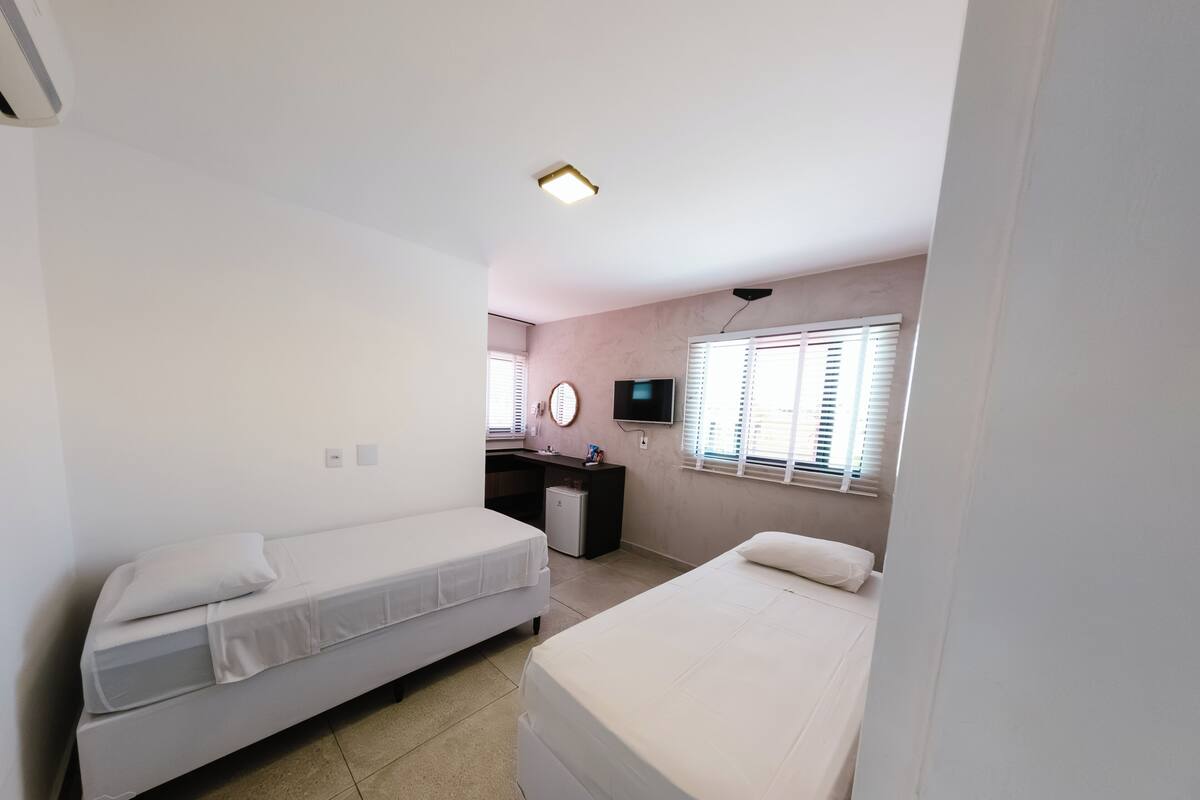 A room with two beds, a desk, a TV, and a window with blinds.