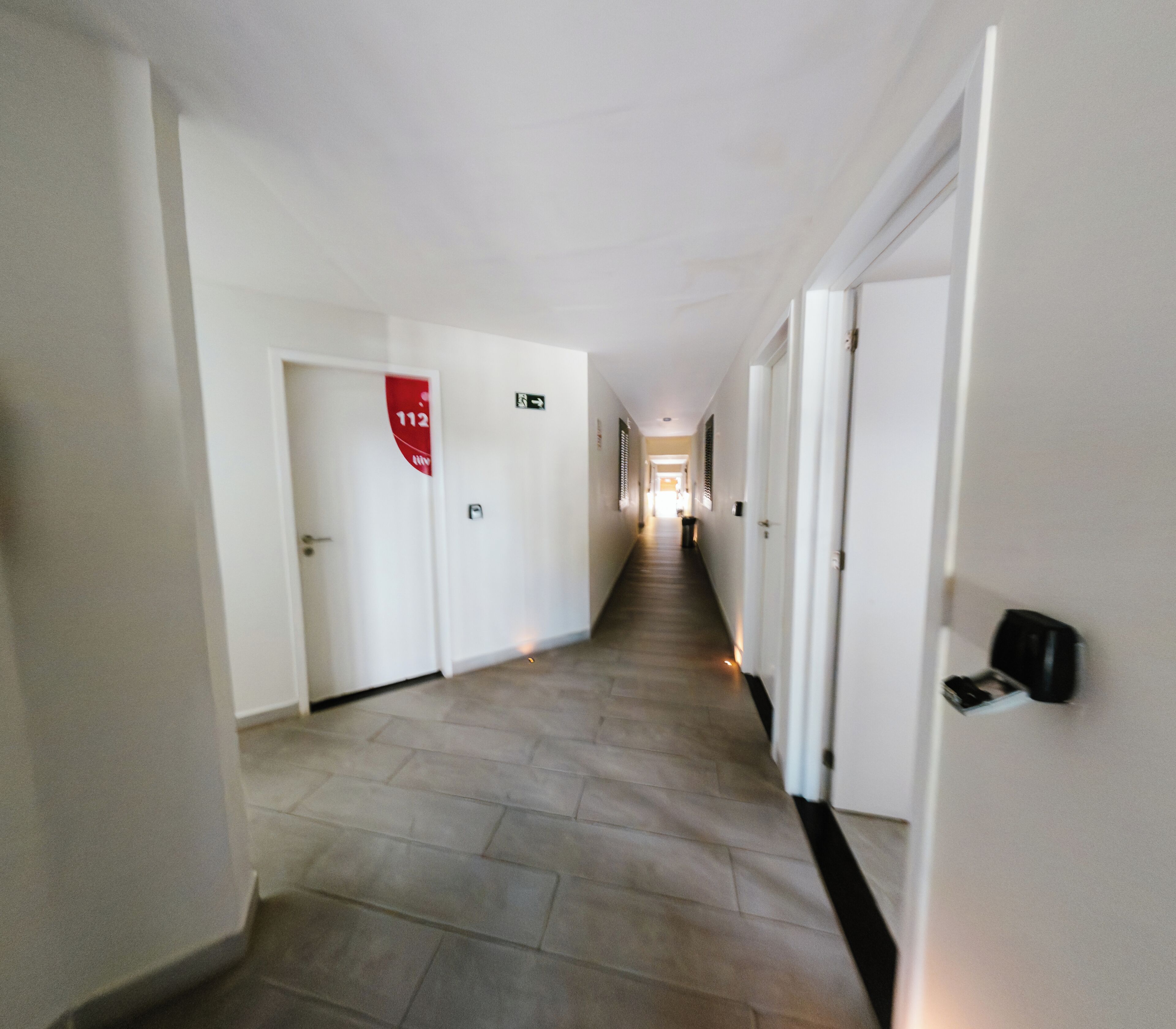 A hotel hallway with white walls, a tiled floor, and doors on both sides.