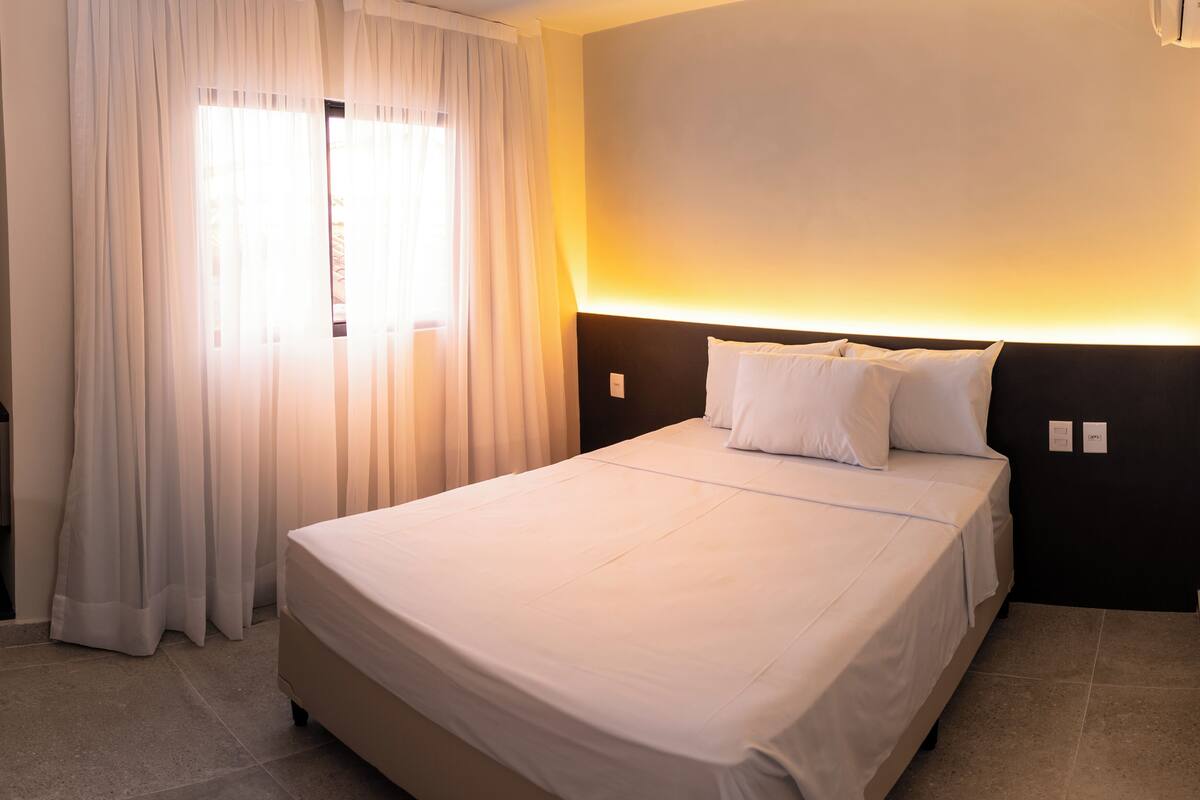 A hotel room with a bed, a desk, and a window with curtains.