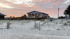 Een strandhuis met terras en overdekte veranda, omgeven door duinen.
