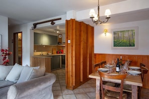 Een eetgedeelte met een houten tafel voor vier personen, een keuken op de achtergrond en een schilderij aan de muur.