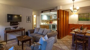 A living room with a sofa, coffee table, TV, and a dining area with a table set for two. - Private terrace, warm & cosy lounge with fireplace (Vaujany)