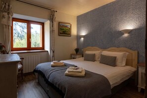 Een slaapkamer met een bed, een raam, een nachtkastje, een lamp en een schilderij aan de muur.