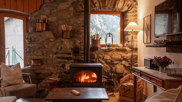 A cozy room with a stone fireplace, a wooden table, a comfortable chair, and a television. - Private terrace, warm & cosy lounge with fireplace (Vaujany)