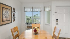 A dining area with a round wooden table, two wooden chairs, a vase with flowers, a framed picture, and a decorative metal piece on the wall. - Windjammer 209 - 2 Bedroom Oceanfront Getaway (St. Augustine)