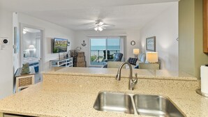A kitchen with a granite countertop, stainless steel sink, and a ceiling fan. - Windjammer 209 - 2 Bedroom Oceanfront Getaway (St. Augustine)