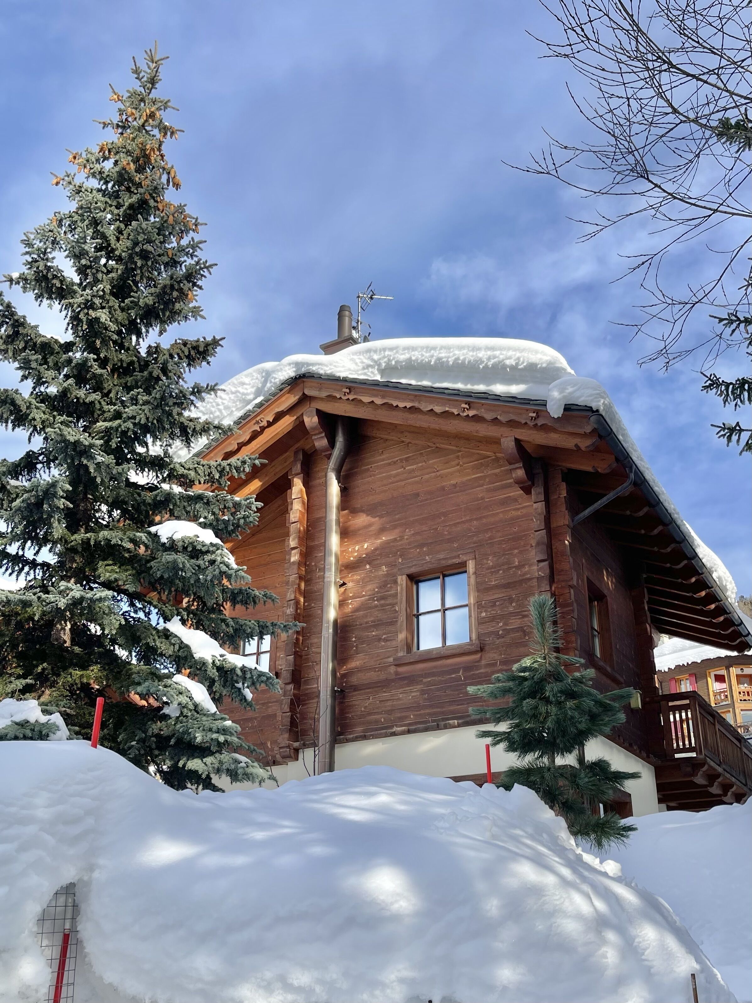 A wooden cabin with a snow-covered roof, a chimney, and a window.