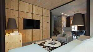 A modern hotel room with a wooden panel wall, a flat-screen TV, a round coffee table with decorative items, a sofa, and a chair. - Chalet Cirmolo (Livigno)
