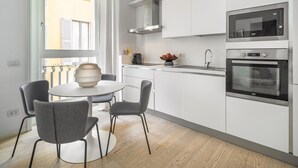 A modern kitchen with white cabinets, a built-in microwave, and an oven. There is a dining area with a round table and two chairs. - Brera Design Apartment R&R (Milano)