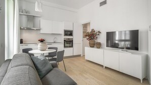 A modern living room with a grey sofa, a dining table with chairs, a kitchen area with white cabinets, a built-in oven, and a flat-screen TV on a white console. - Brera Design Apartment R&R (Milano)