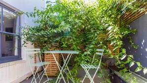 A small outdoor area with a table and chairs, surrounded by a wooden fence and a climbing plant.