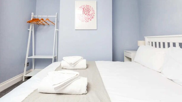 A hotel room with a bed, a white nightstand, a white dresser, a white wardrobe, and a framed artwork on the wall.