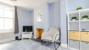A modern living room with a grey carpet, a white entertainment unit with plants, a beige armchair, and a fireplace.