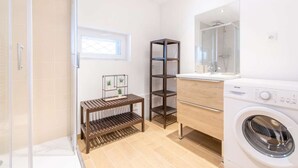 A modern bathroom with a glass shower enclosure, a wooden bench with shelves, a white washing machine, and a mirror above the sink. - Studio Blancarde 1 (Marseille)