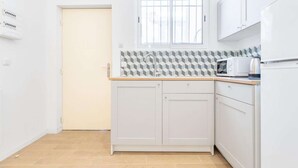 A compact kitchen with white cabinets, a microwave, and a kettle on the countertop. - Studio Blancarde 1 (Marseille)