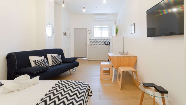 A compact living space with a sofa, a dining table, a TV, and a kitchenette. - Studio Blancarde 1 (Marseille)