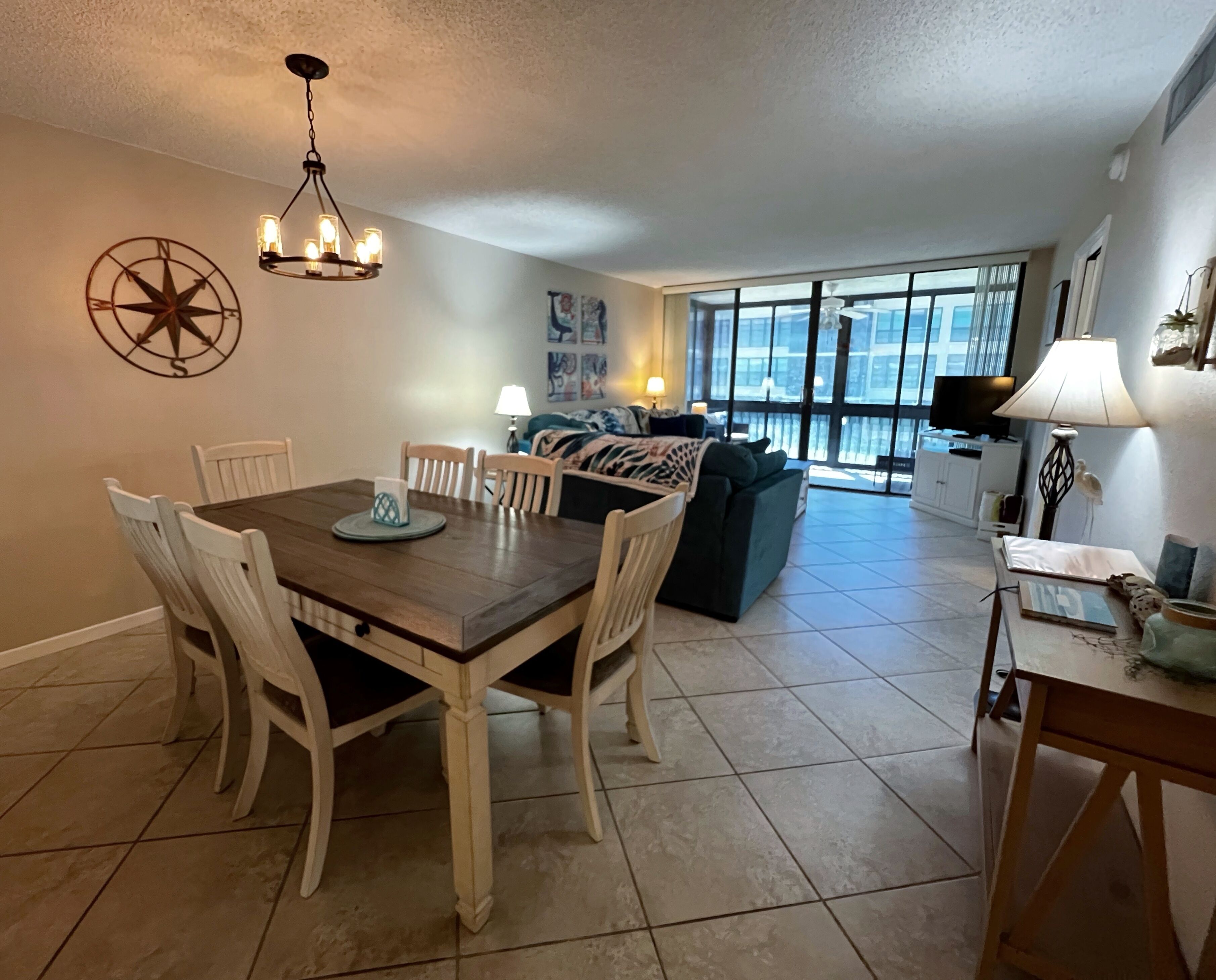 A dining area with a wooden table and white chairs, a sofa, and a TV in the background.