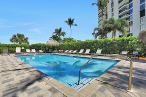 A swimming pool with lounge chairs and palm trees. - Beachfront Condo | Pools, Tennis Courts & Gym (Marco Island)