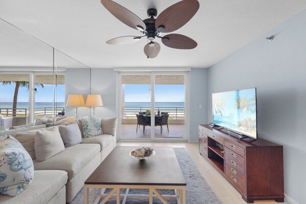 A modern living room with a sofa, coffee table, TV, and a balcony with a view of the ocean.