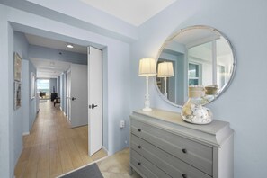 A hallway with a light blue wall, a wooden floor, a white door, and a dresser with a mirror and lamps.