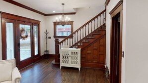Un vestíbulo amplio con una escalera de madera, un candelabro y una consola blanca.